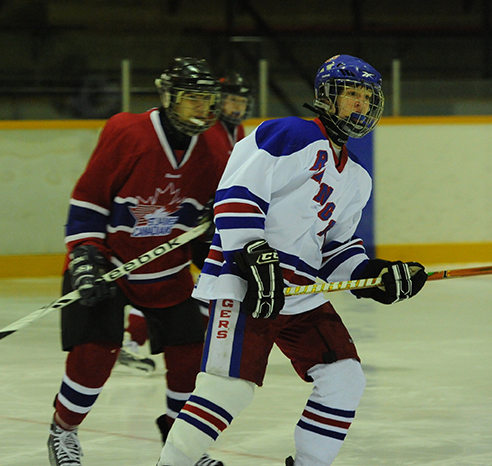 A teenage hockey player skates in front of a player from the other team.