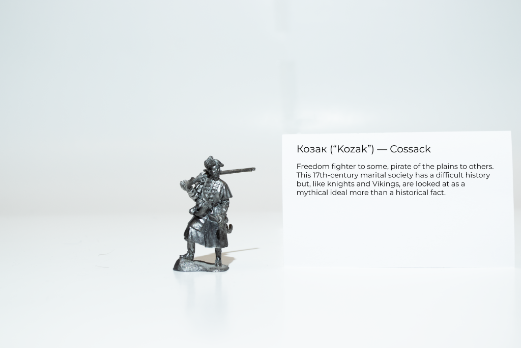 Museum-style photo of a small, pewter figurine. The figurine is shaped like a Ukrainian Cossack warrior. A card beside the figurine reads "Cossack: Freedom fighter to some, pirate of the plains to others. This 17th-century marital society has a difficult history but, like knights and Vikings, are looked at as a mythical ideal more than a historical fact."