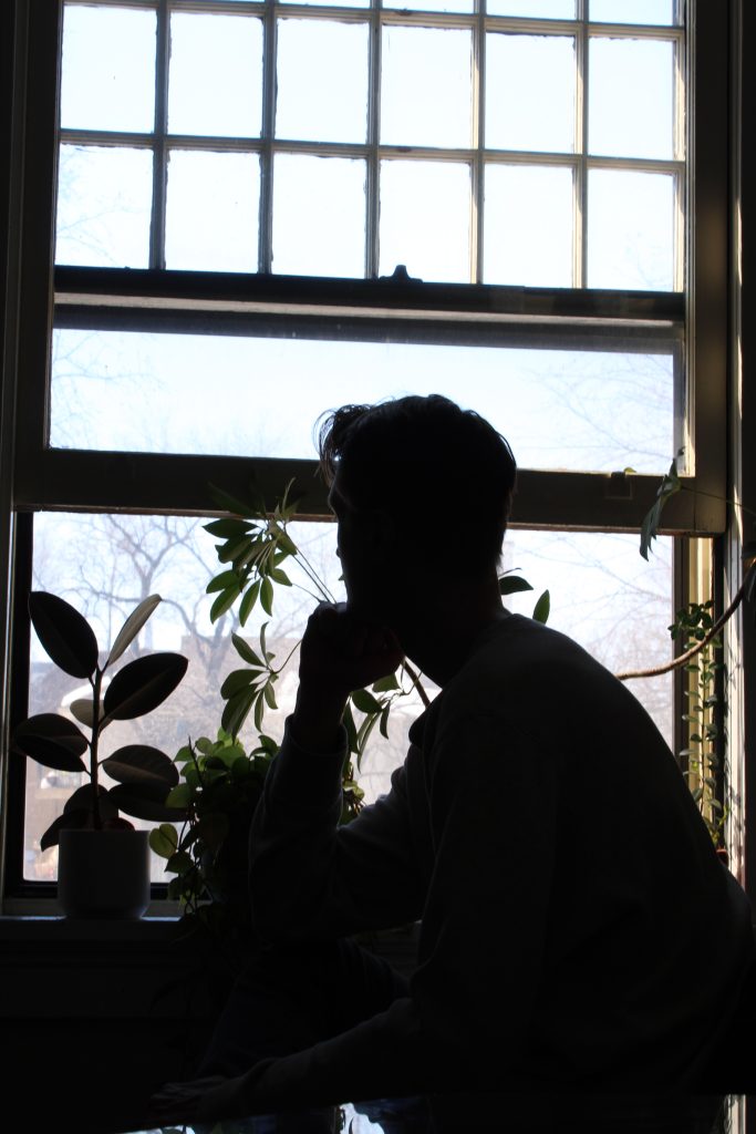 This image shows the dark silhouette of Eric as he looks out of his apartment window. 